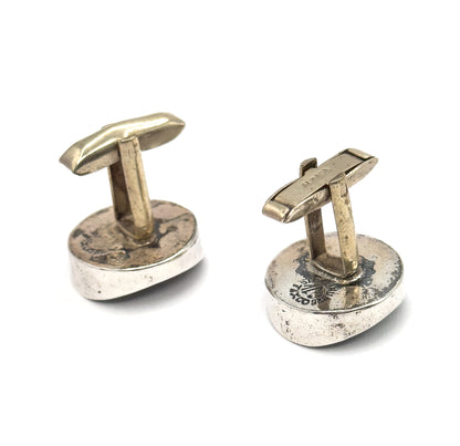 Reverse view of both cufflinks, the rounded sterling silver backs facing up with stamped marks visible and each hinged toggle bar standing upright on its post.