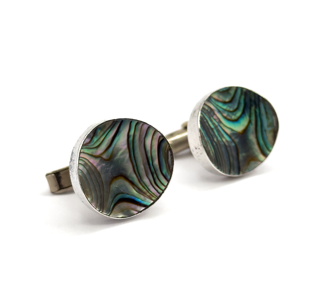 Close three-quarter view of both faces together, the concave abalone showing rippling green, pink and blue banding inside its sterling silver bezel, one toggle bar jutting out at left.