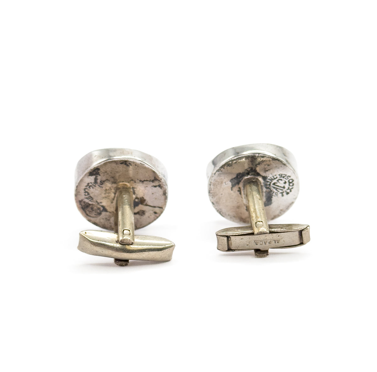 Both cufflinks stood side by side on their toggle bars, the rounded sterling silver backs facing forward with stamped marks and patina showing across each.