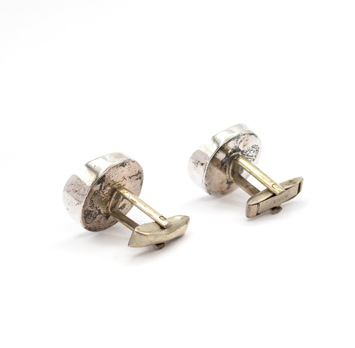Low three-quarter view from behind the pair, the rounded sterling silver backs angled away while both posts and hinged toggle bars swing down and forward toward the camera.