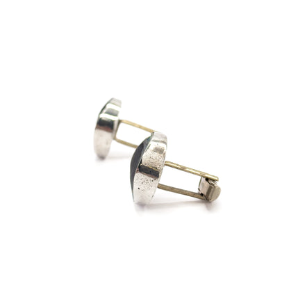 Edge-on profile of the pair, the sterling silver faces seen as slim curved discs in silhouette with both posts and hinged toggle bars reaching out to the right.