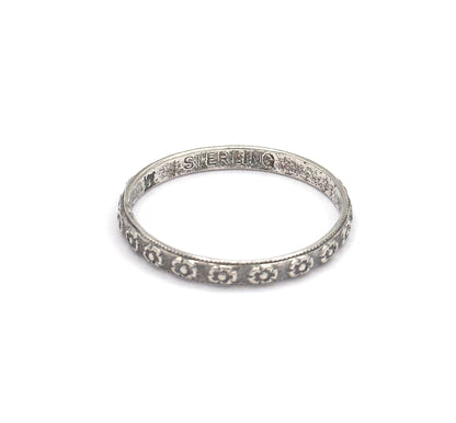 The band lies on a white background, tilted to show the flower-stamped shank in front and a stamped word inside the back of the hoop, patina darkening the recesses.