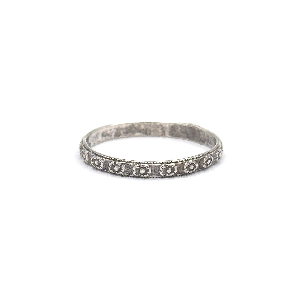 Standing upright on a plain white background, the band faces the camera head-on so the full row of stamped flowers runs along the front of the shank, patina deepening each petal.