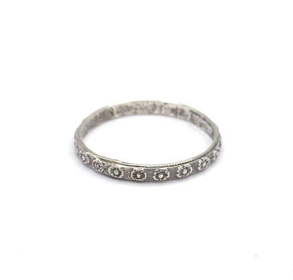 Seen from a low, near-level angle, the hoop appears as a slim ellipse so the narrow depth of the shank is clear, with the stamped flowers catching light along its lower front edge.