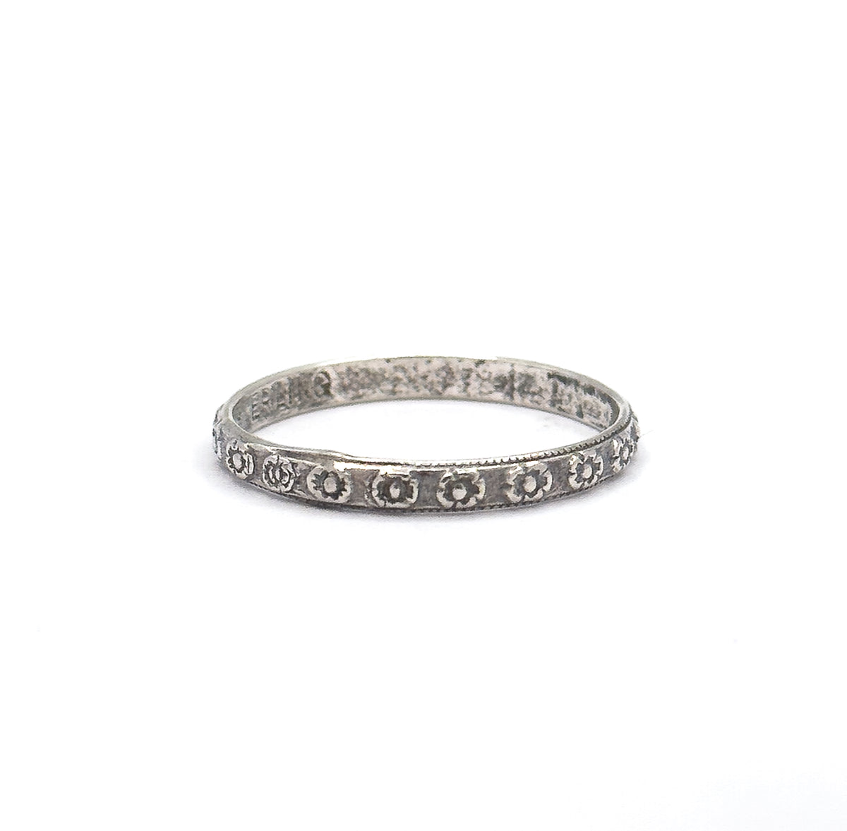 Pulled back so the band sits small in a wide white frame, conveying its slender scale, with the row of stamped flowers across the front and faint markings inside the back of the hoop.