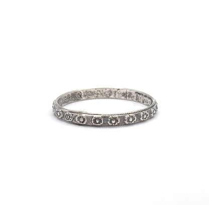 Pulled back so the band sits small in a wide white frame, conveying its slender scale, with the row of stamped flowers across the front and faint markings inside the back of the hoop.