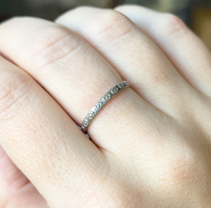 A slim sterling silver band with a row of small flowers along its face, shown on a finger in close-up so its narrow profile sits flush against the skin.
