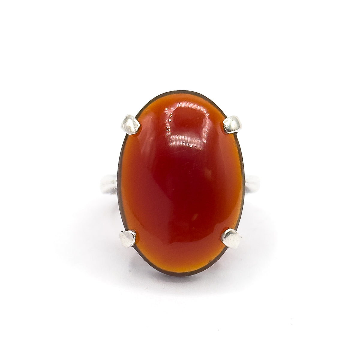 Close front-on crop filling the frame with the oval red cabochon, its glossy domed surface catching a bright highlight, four silver prongs at the corners and only a sliver of shank behind.