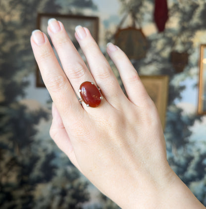 The whole back of the hand is shown against a blurred painted backdrop, the ring on the ring finger giving a sense of its scale across the finger.