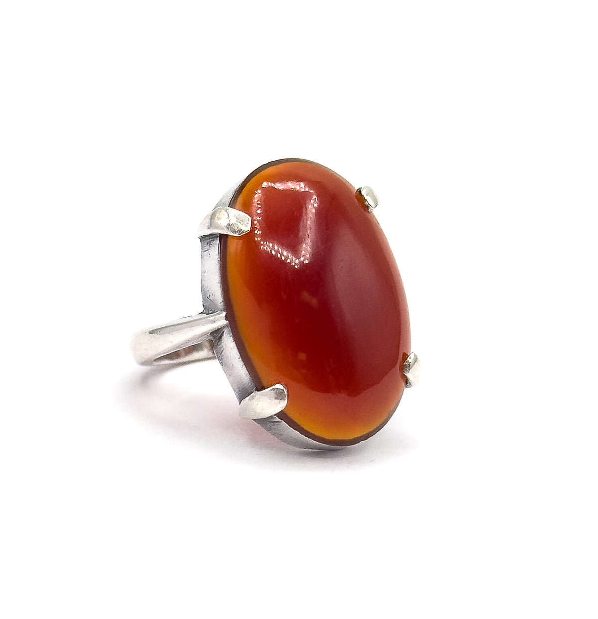 The ring alone on a white background in three-quarter view, the domed oval red cabochon angled toward the viewer with its four sterling silver prongs and the shank curving away behind.