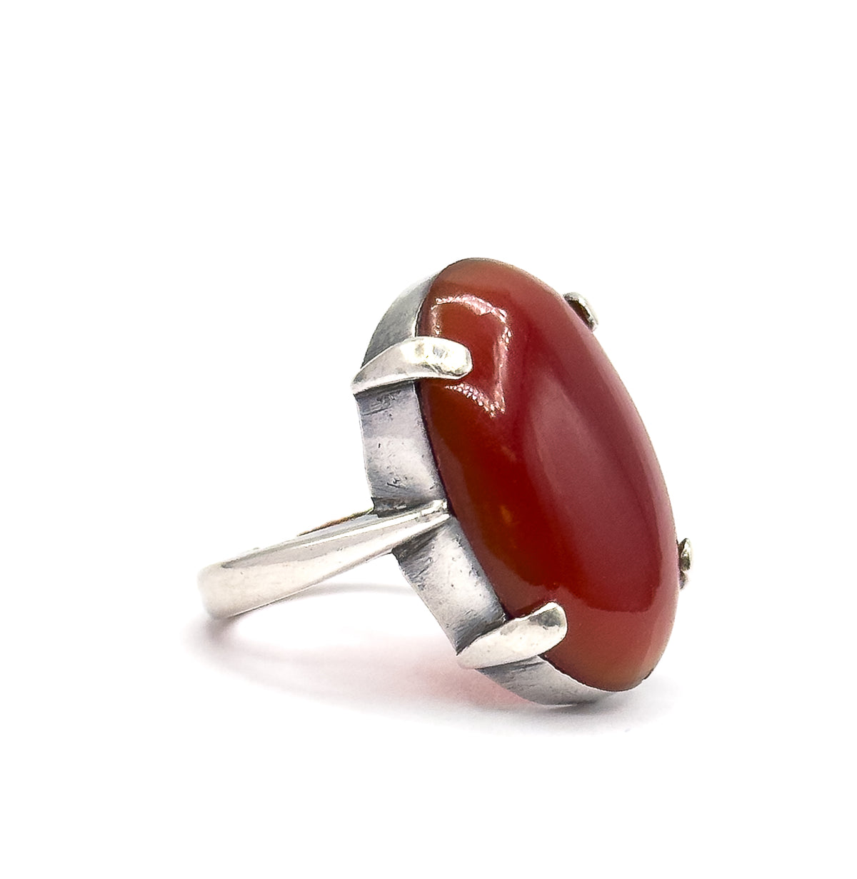 Side-on view against white, the tall dome of the red cabochon rising from a deep bezel wall with the prongs seen in profile and the shank sweeping low to the left.