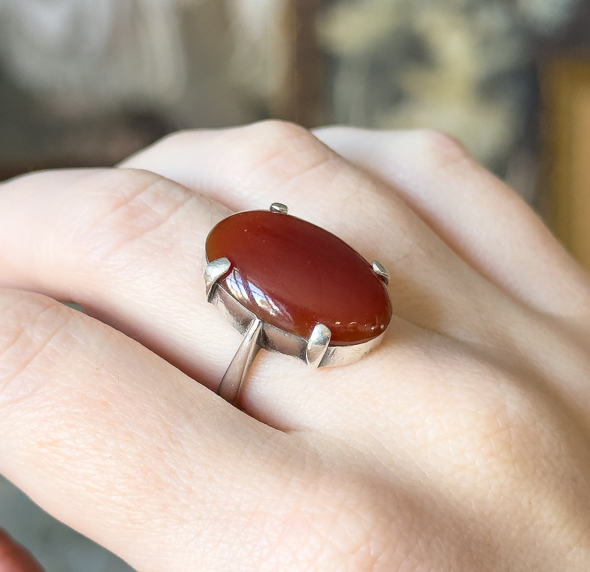 Mid-century red stone ring in sterling silver, shown on a finger, its large oval deep red cabochon held by four prongs above a slim plain shank.