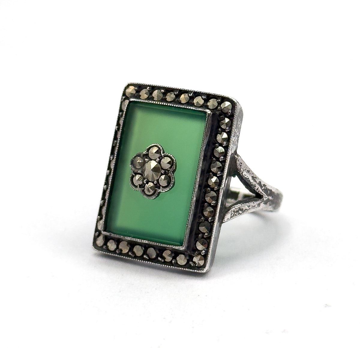 Front-facing view with the ring standing upright, the full green chrysoprase rectangle, its marcasite flower centre and complete halo square to the camera, the split shoulders visible at right.