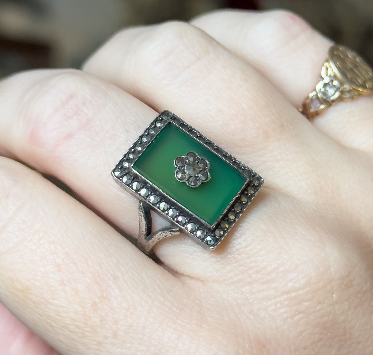 Art Deco chrysoprase and marcasite cocktail ring in sterling silver, shown on a finger, its rectangular green stone bezel set with a marcasite flower at centre and a marcasite halo around it.