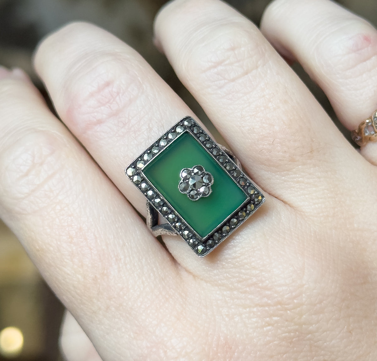 Close view of the ring shown on a finger, with the darkened silver shank and the ring's raised rectangular face visible against the skin, giving a sense of its size.