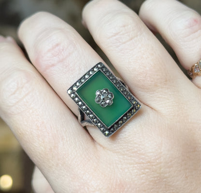 Close view of the ring shown on a finger, with the darkened silver shank and the ring's raised rectangular face visible against the skin, giving a sense of its size.