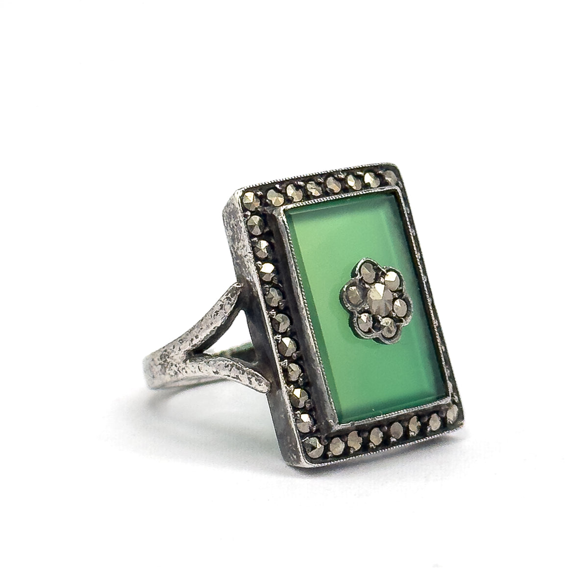 Standing alone on a plain white background at a three-quarter angle, showing the split shank rising to the deep bezel and the marcasite halo framing the green rectangular stone.