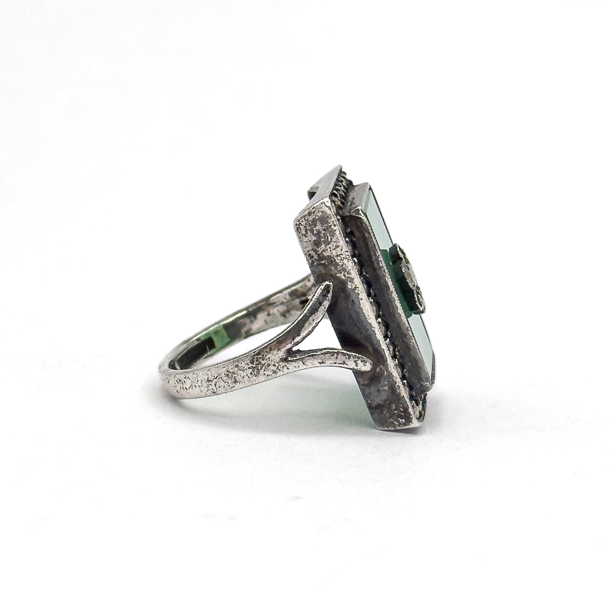 Side profile against white, showing the tapering sterling silver shank forking into a split gallery beneath the deep bezel, with the green stone's edge in view.