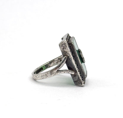 Side profile against white, showing the tapering sterling silver shank forking into a split gallery beneath the deep bezel, with the green stone's edge in view.