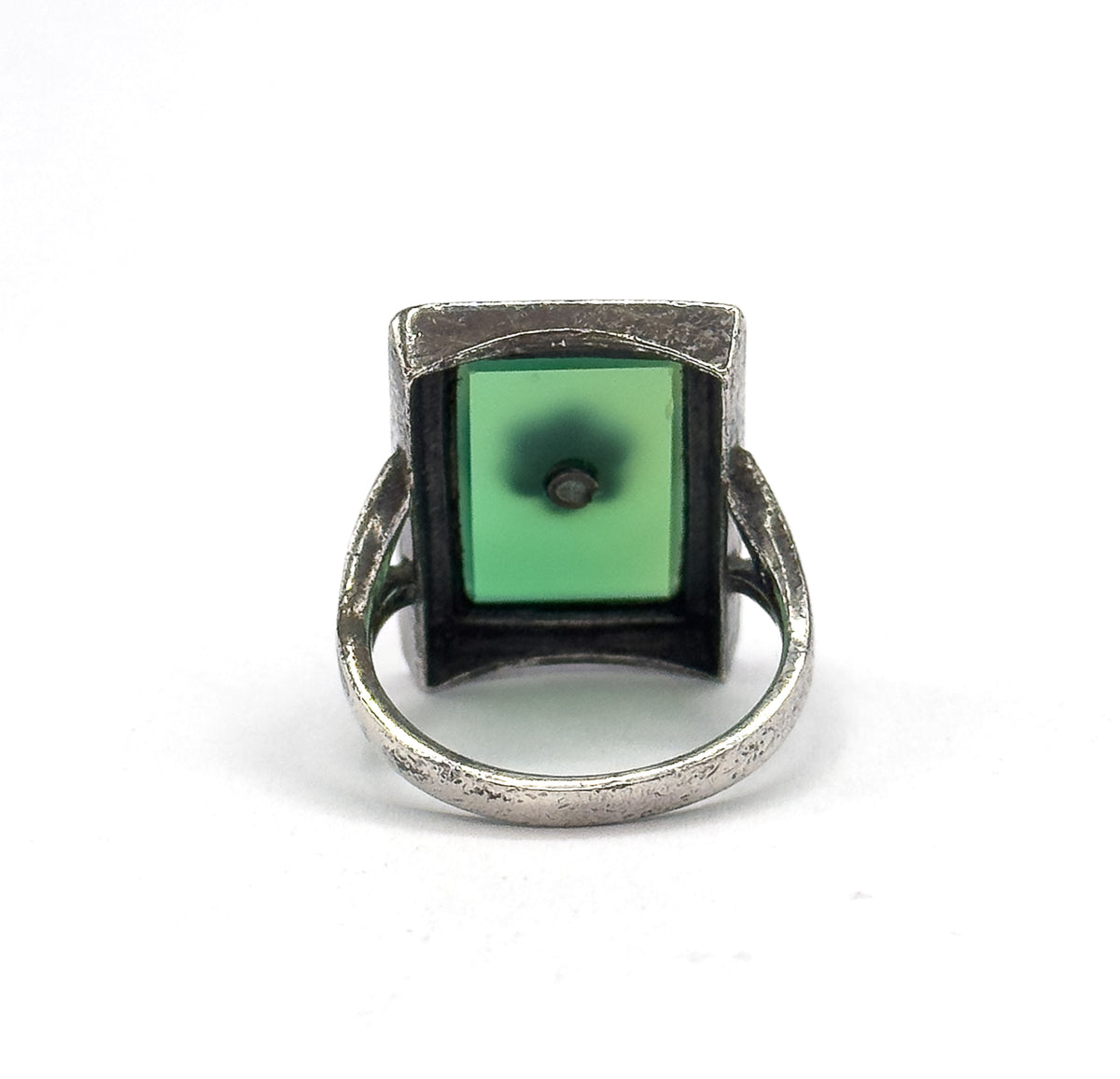 Almost the same view with slightly different angle, looking straight into the open back of the bezel so the green stone's underside and its tiny central drill point fill the square frame.