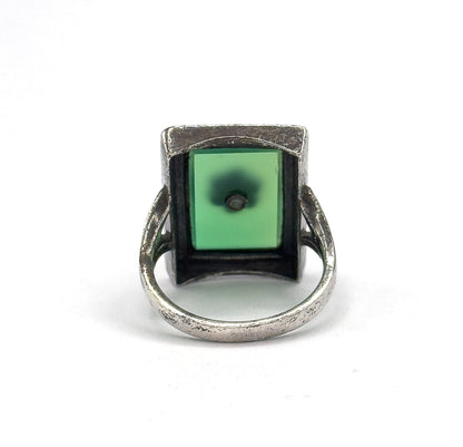 Almost the same view with slightly different angle, looking straight into the open back of the bezel so the green stone's underside and its tiny central drill point fill the square frame.
