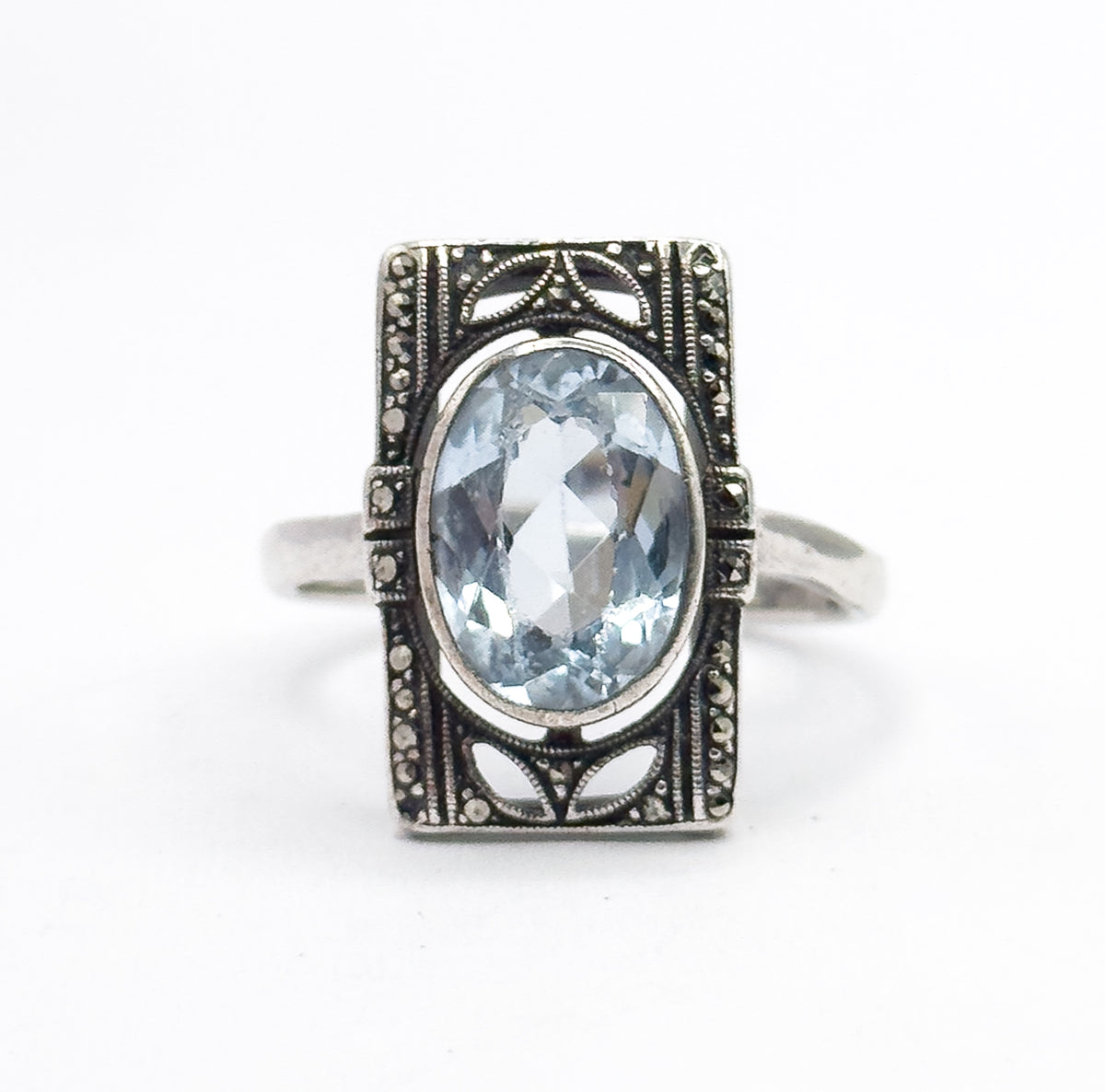Straight-on front view of the whole face flat to the camera, the oval icy blue stone bezel-set at the center with marcasite-set borders and petal-shaped openwork above and below.