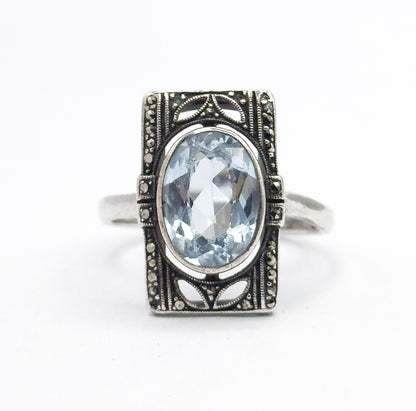 Straight-on front view of the whole face flat to the camera, the oval icy blue stone bezel-set at the center with marcasite-set borders and petal-shaped openwork above and below.