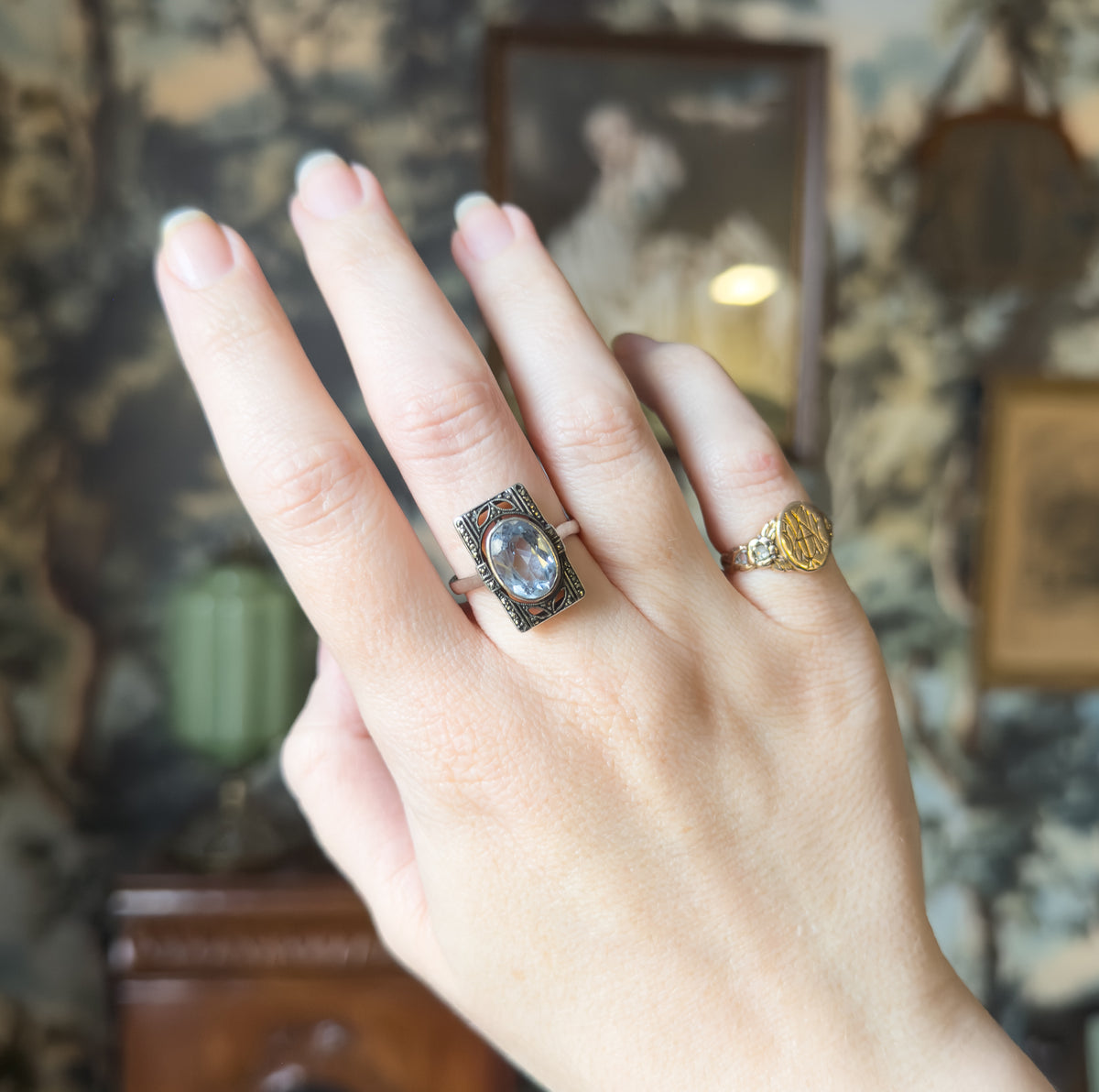 Shown on a raised hand with fingers spread, the rectangular face sits upright on the ring finger, its icy blue stone catching light beside a plain band on the next finger.