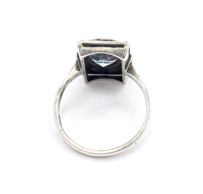 Upright head-on view through the open shank from behind, so the back of the oval icy blue stone shows through the gallery opening beneath the bezel and rectangular face.