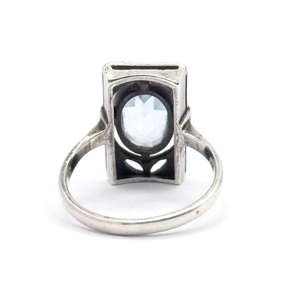 Reverse of the ring laid flat, the full circle of the slim shank framing the gallery's petal-shaped cut-outs and the open back of the bezel where the oval icy blue stone shows through.