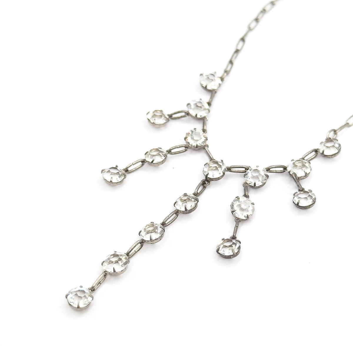 Angled view with the fringe set diagonally across the white background, the chain running off to the upper corners and the longest strand of paste stones trailing toward the lower left.