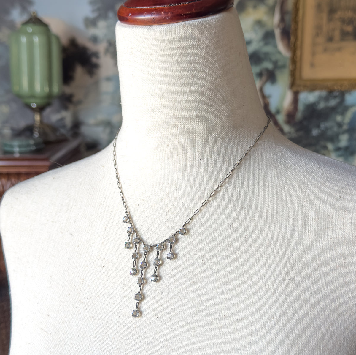 Angled view from the side, the fine chain curving over the bust form's shoulder while the paste fringe drops hang free below the neckline.