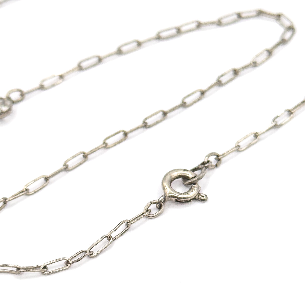 Close view of the chain's elongated oval links against white, following them to the round spring ring clasp and its small jump ring at the back of the necklace.