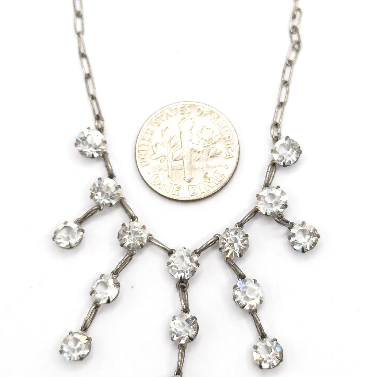 A small coin rests on the white background beside the fringe to show scale, the branching paste strands spreading across and below it from the two chain ends.