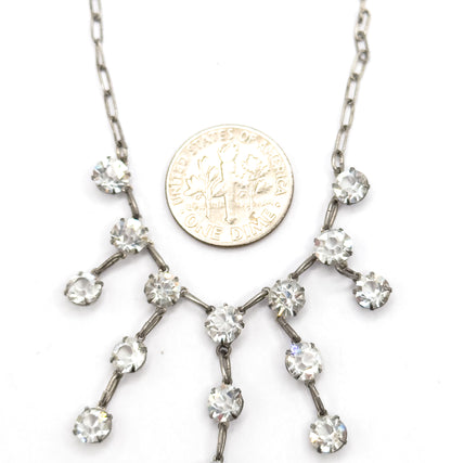 A small coin rests on the white background beside the fringe to show scale, the branching paste strands spreading across and below it from the two chain ends.