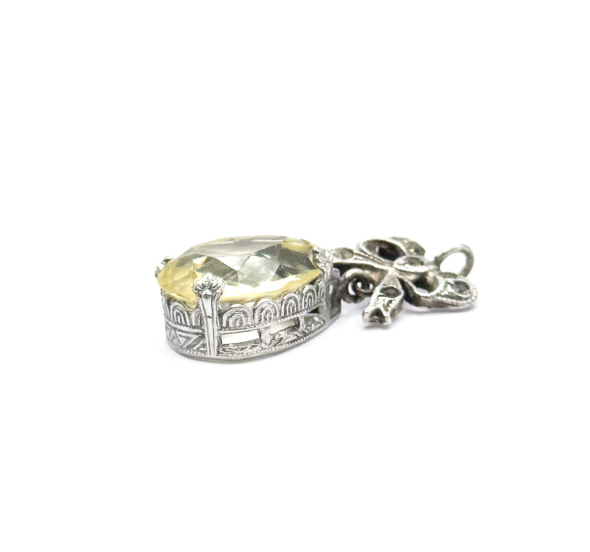 Side-on view against white showing the depth of the teardrop bezel and its arched, pierced gallery wall, with the bow and round bail lying flat to the right.