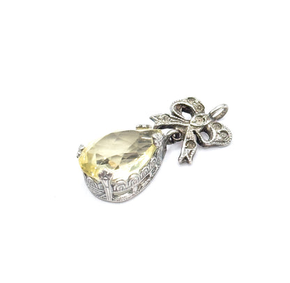 Tilted three-quarter view from above, the lime-coloured teardrop facets catching light while the sterling silver bow and round bail angle away to the upper right.