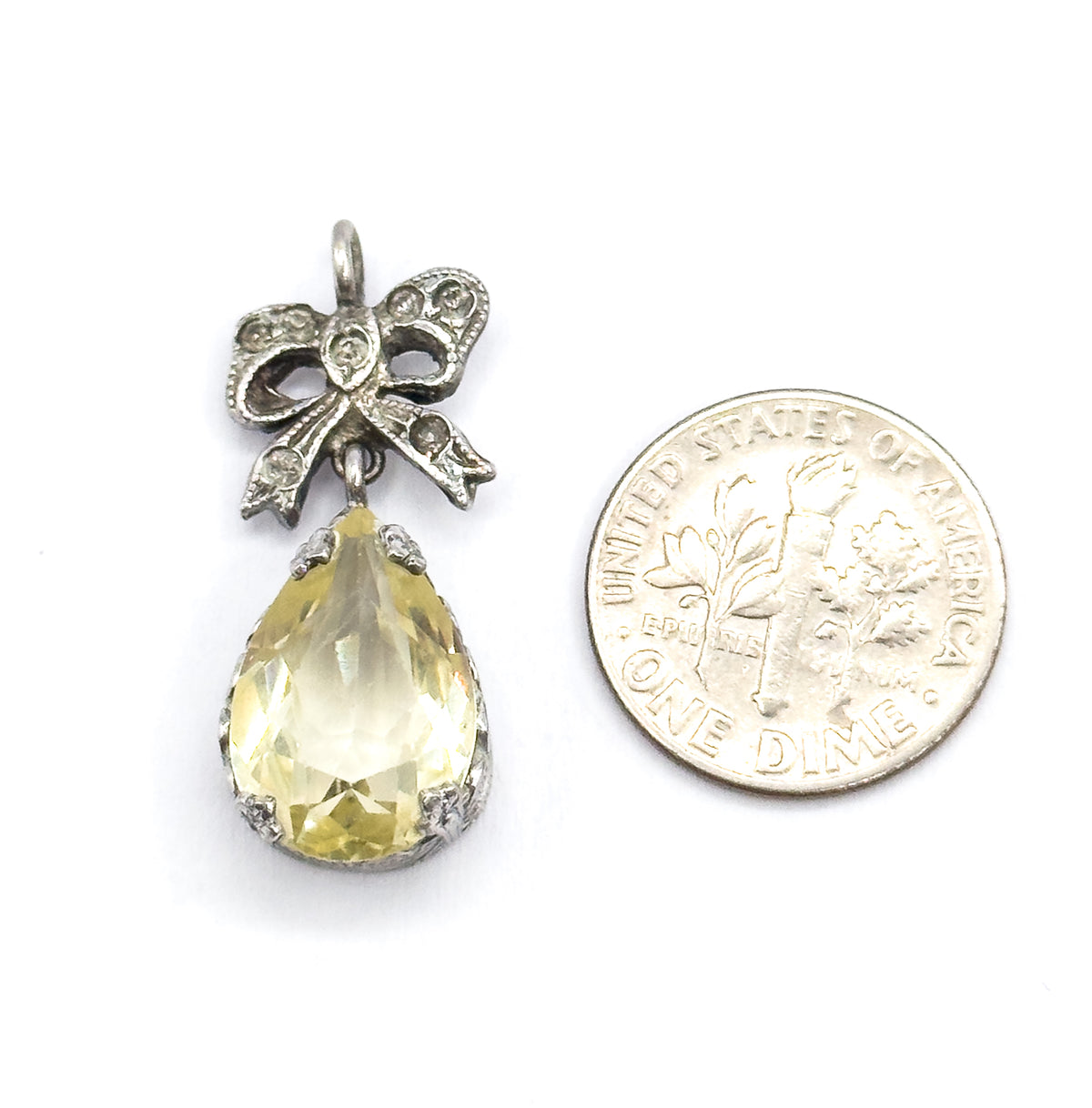 Front view beside a dime for scale, the whole pendant standing a little taller than the coin, with the lime-coloured teardrop in its prong-set bezel below the sterling silver bow and round bail.