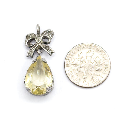 Front view beside a dime for scale, the whole pendant standing a little taller than the coin, with the lime-coloured teardrop in its prong-set bezel below the sterling silver bow and round bail.