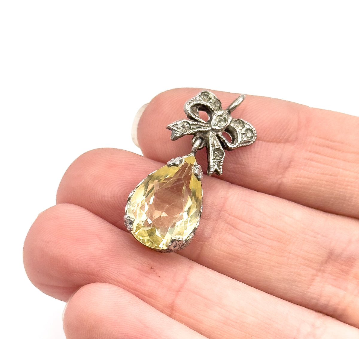 Sterling silver pendant with a lime-coloured teardrop stone in a pronged setting below a small bow motif, shown resting on fingertips to convey its petite size.
