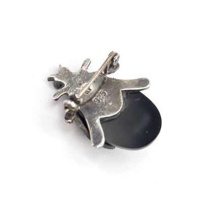 The reverse view on a white background, showing the pin stem, hinged catch, maker's marks on the silver back and the domed black cabochon curving out beneath.
