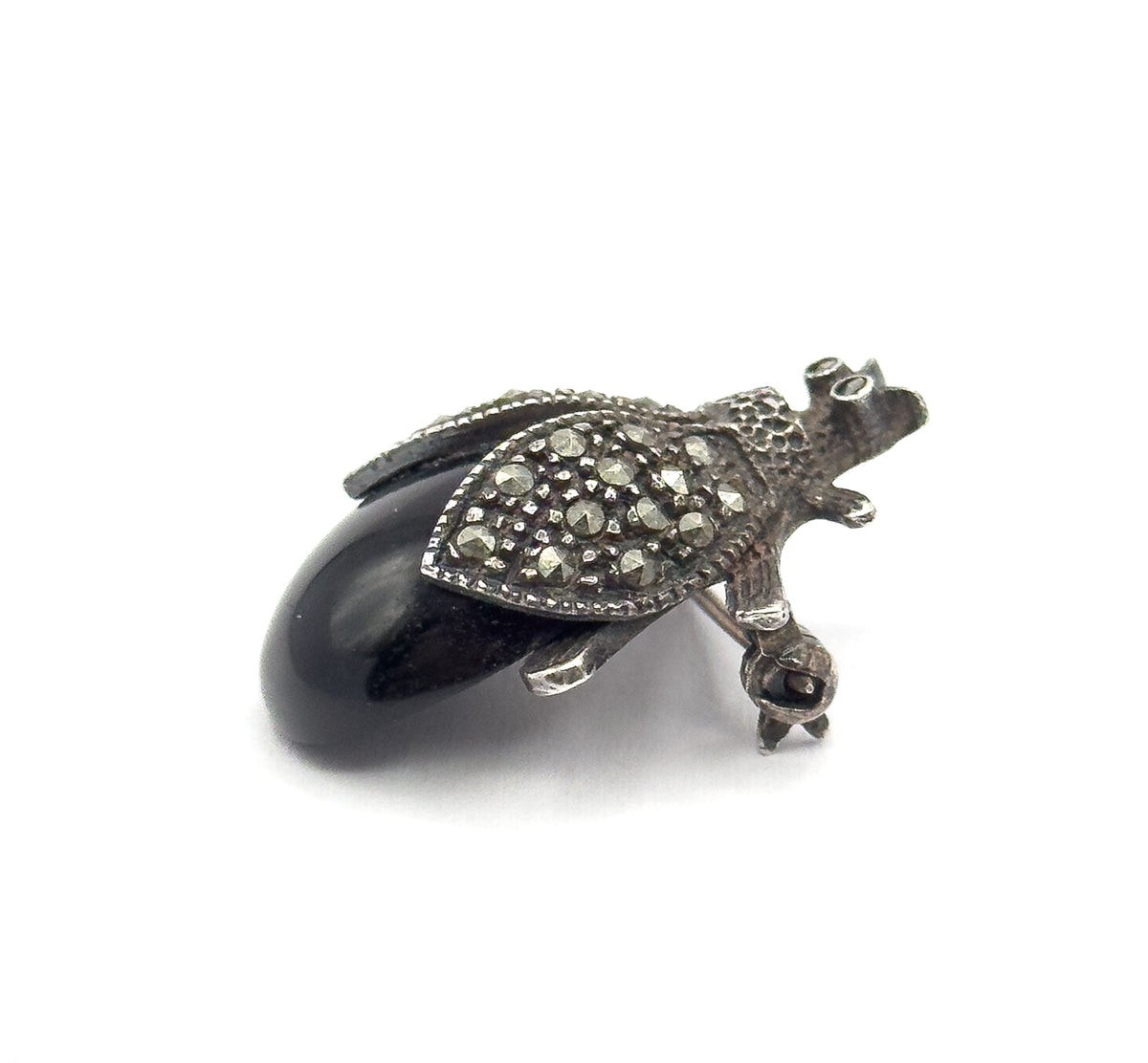 Angled three-quarter view on white, the domed black cabochon rising in profile beside one small-stone-set wing, with the textured head, tiny legs and the pin stem visible behind.