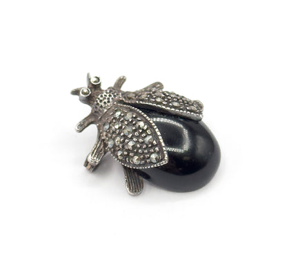 Close top view on white, the head's two tiny round eye stones and slender antennae now clear, with both small-stone-set wings swept back over the smooth black cabochon body.