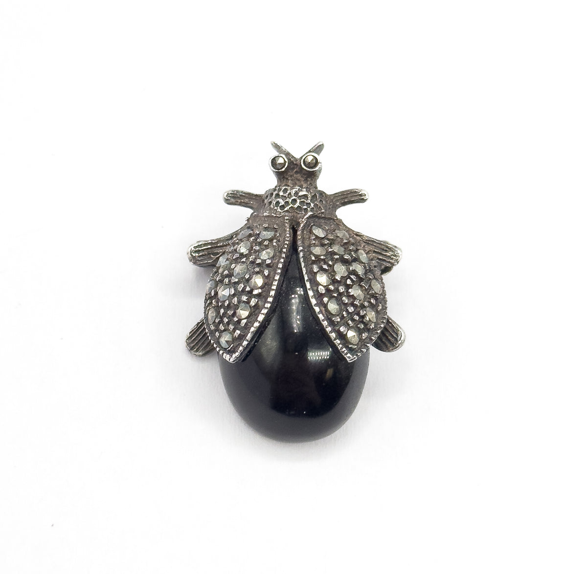 Straight-on top view filling the frame, the whole insect silhouette centred with three tiny legs splayed on each side and a bright highlight gleaming across the smooth black cabochon body.