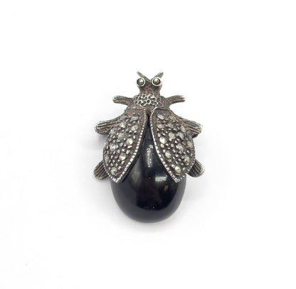 Straight-on top view filling the frame, the whole insect silhouette centred with three tiny legs splayed on each side and a bright highlight gleaming across the smooth black cabochon body.