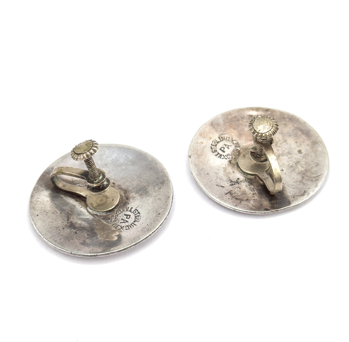 Both discs seen from behind at an angle, each curved sterling back carrying a ridged screwback knob, threaded post and flat paddle arm, with circular stamps on both.