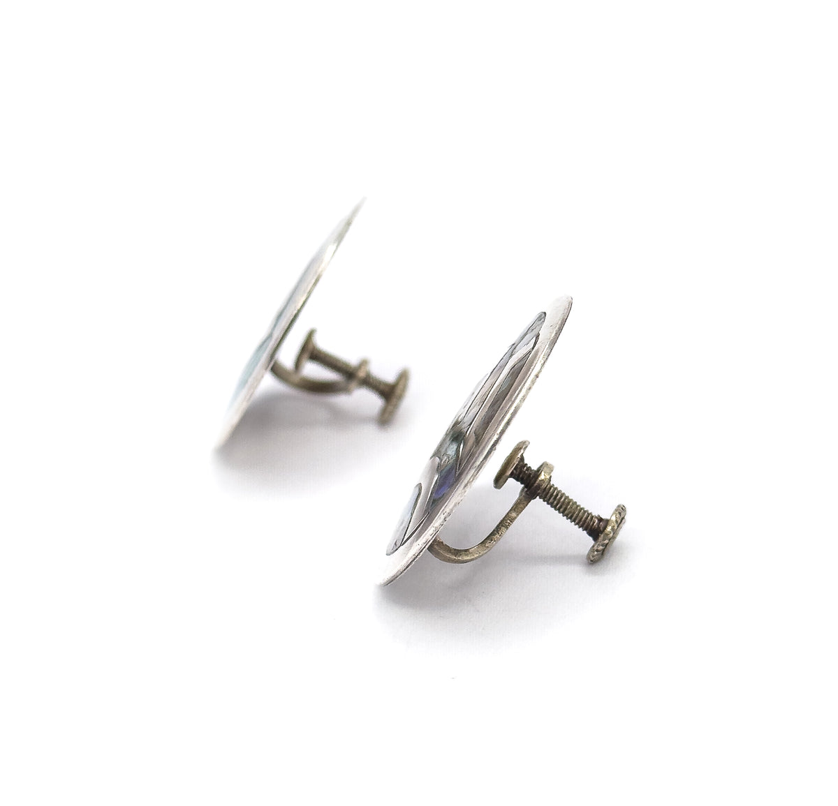 Edge-on view of both earrings, the discs tilting away as thin silver profiles while the threaded screwback posts and their flat paddle ends project sideways toward the viewer.