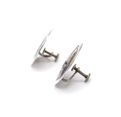Edge-on view of both earrings, the discs tilting away as thin silver profiles while the threaded screwback posts and their flat paddle ends project sideways toward the viewer.
