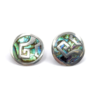 Both discs face up and close together without the coin, each sterling scroll forming an angular stepped spiral across abalone shell that flashes green, blue and violet.