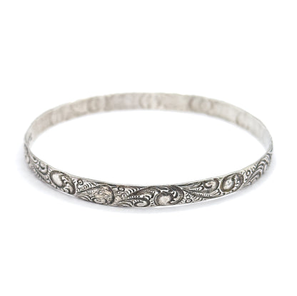 The whole sterling silver bangle seen from a low angle on a plain background, the full oval standing closed and upright with scrollwork sharp across the near rim.